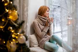 woman-holding-cup-wathing-from-window-near-christmas-tree